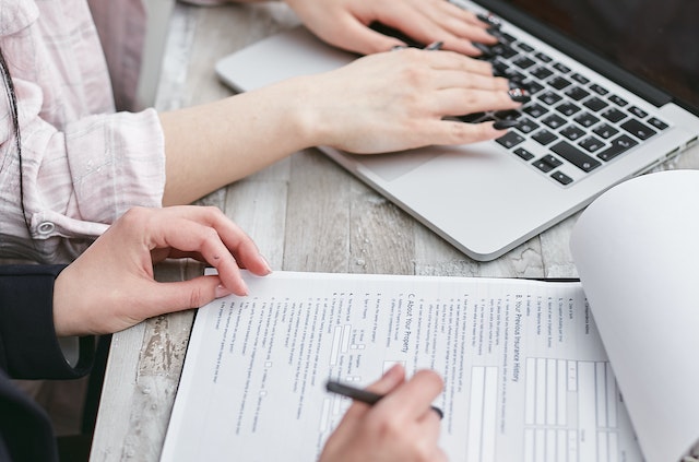 One set of hands typing on a silver laptop, another filling out a form